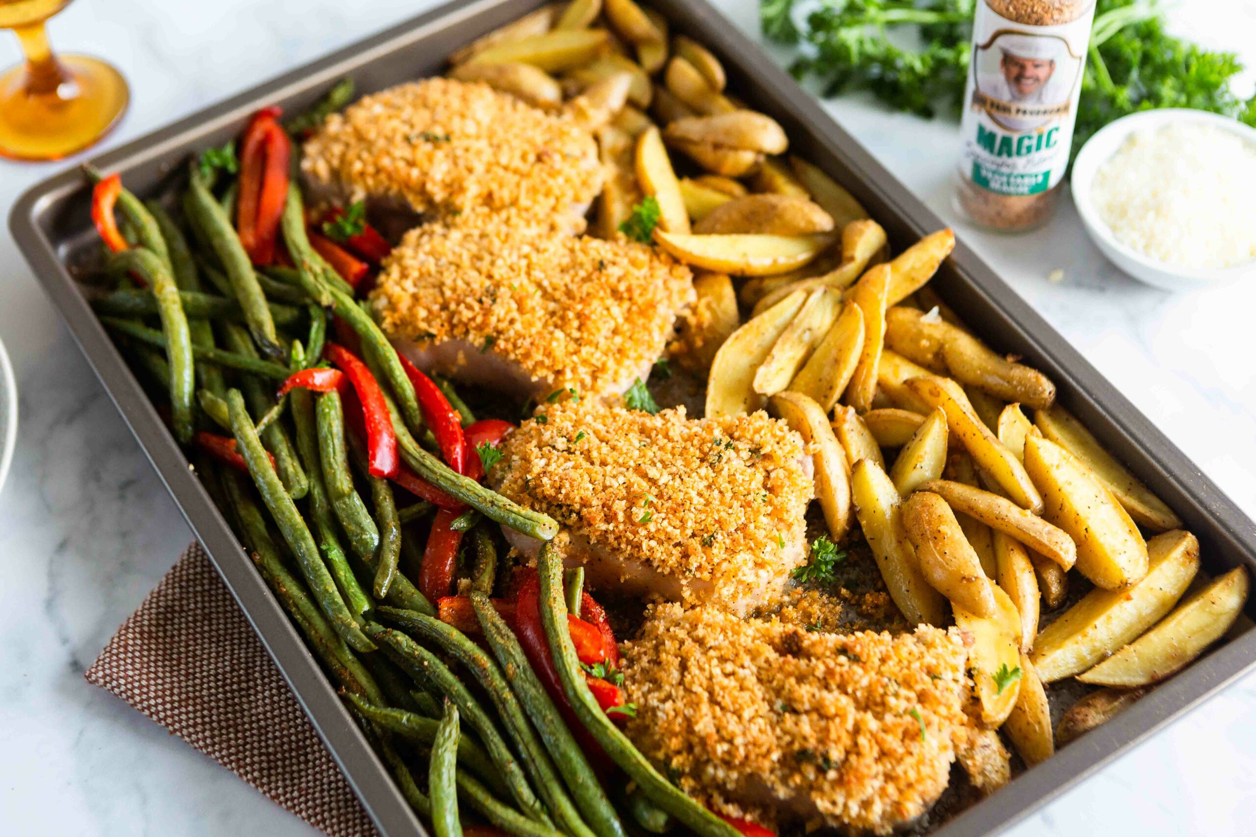 a shet pan of sheet pan parmesan pork chops including the sides of french fries and green beans and red pepers to be baked