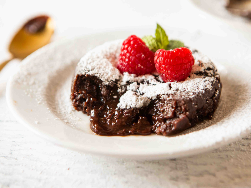 a plate of chocolate lava cake topped with powered sugar and 2 raspberries