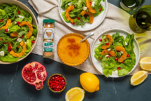 Lemon Vinaigrette in a small dish next to salad, lemons, pomegranates, and vegetable magic