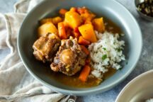 a bowl of slow cooker cooked oxtail and vegetable soup with a side of rice