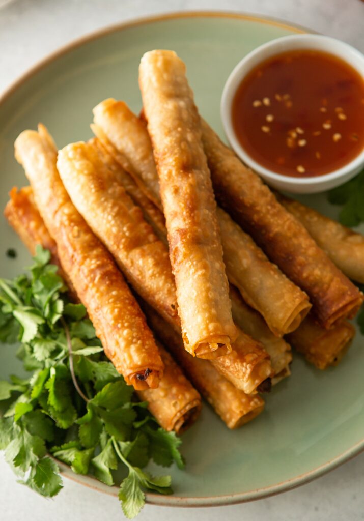 a close up of a palte of lumpia and thai chili sauce in a dipping cup