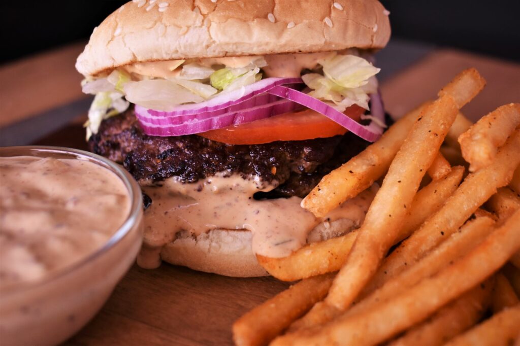 a burger with magic burger sauce dripping out of it next to a cup of the magic burger sauce and some seasoned french fries