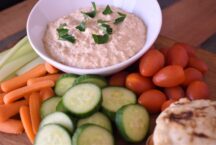 a bowl of caramelized onion dip surrounded by celery, carrots, cherry tomates, pita bread and zucchini for dipping