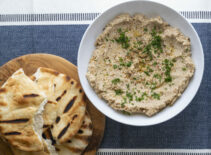 a bowl of cauliflower hummus with salt free sugar free magic seasoning blend next to a cutboard of pita bread