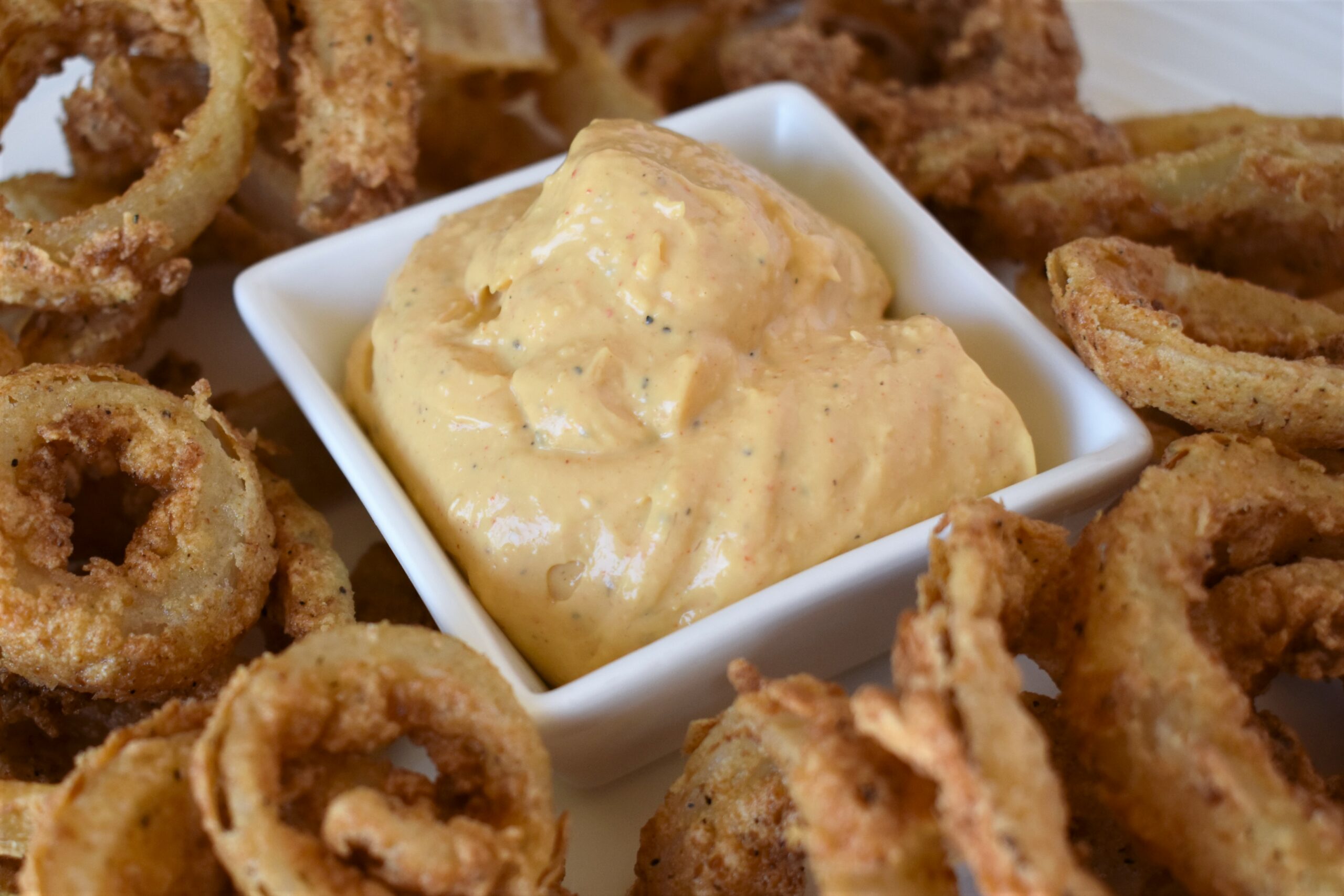 a close up of a cup of aioli surrounded by onion rings
