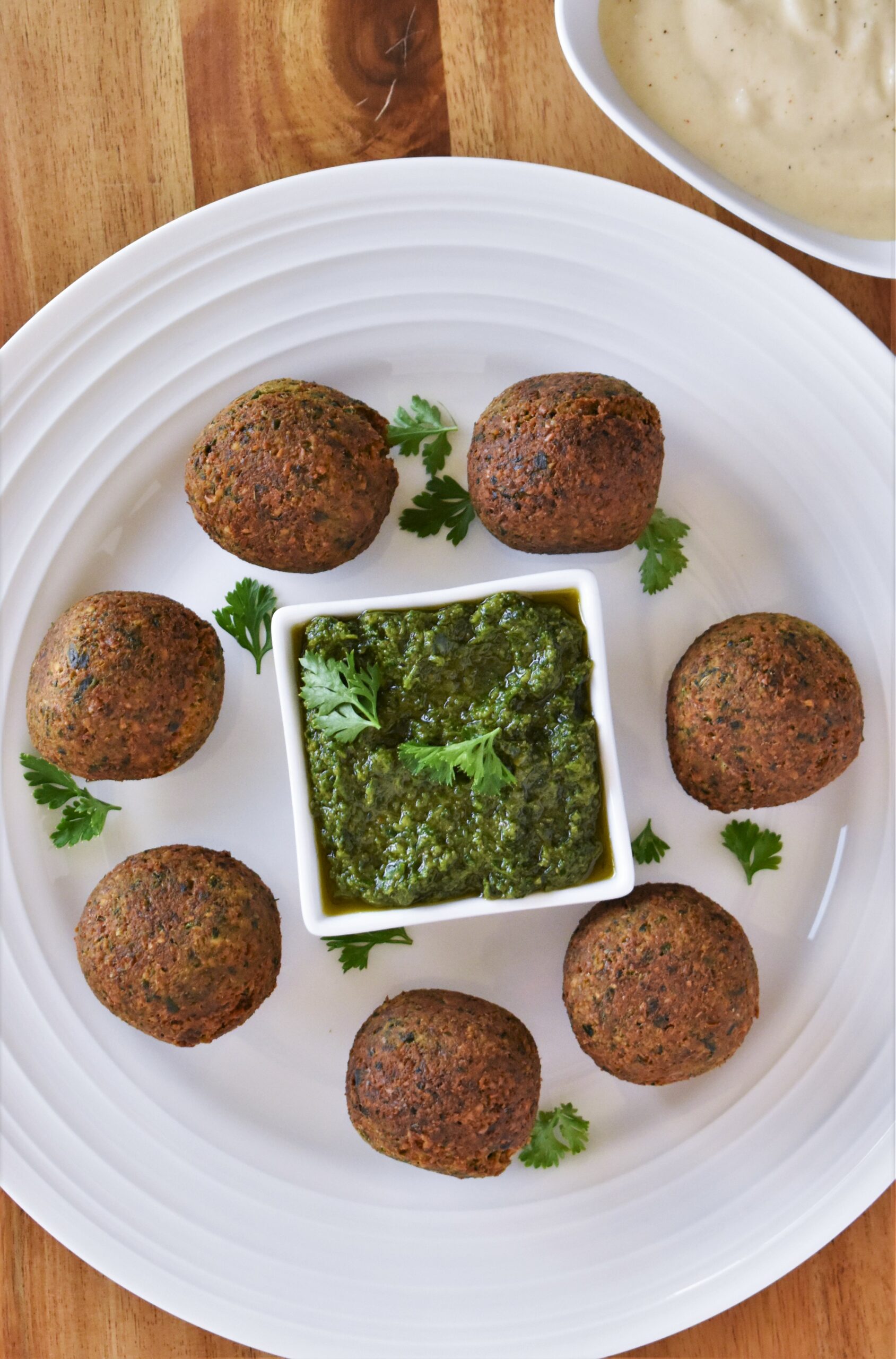 a plate with 8 falafel balls surrounding a pesto filled dipping cup