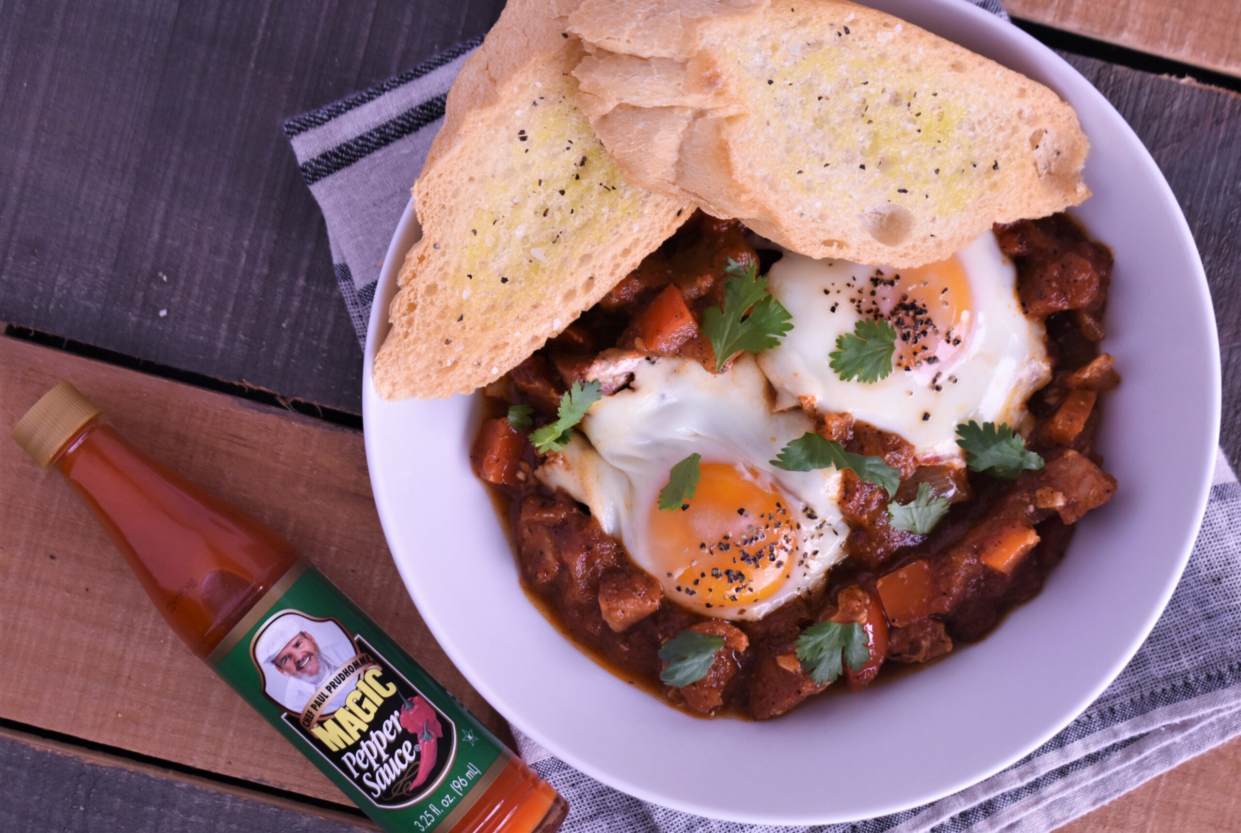 a plate of shashuka with andouille smoked sausage with 2 pieces of bread on the side