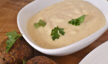 a close up of a bowl filled with tourn (lebanese garlic sauce) next to 2 falafels balls