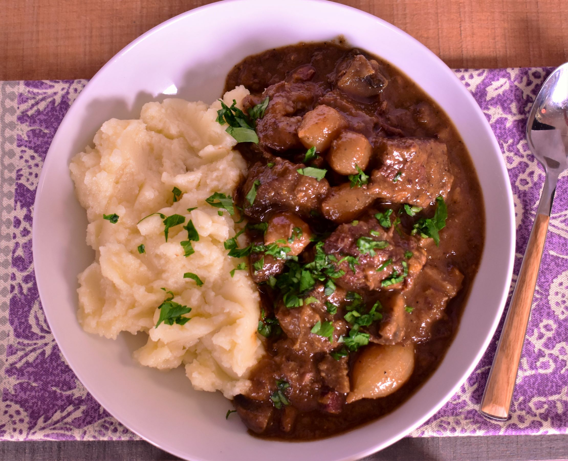 a plate of beef boeuf bourguignon with a side of mashed potatos
