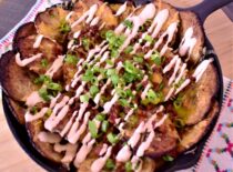 a cast iron skillet of spicy irish nachos drizzled with bacon bits, white sauce, and green onions