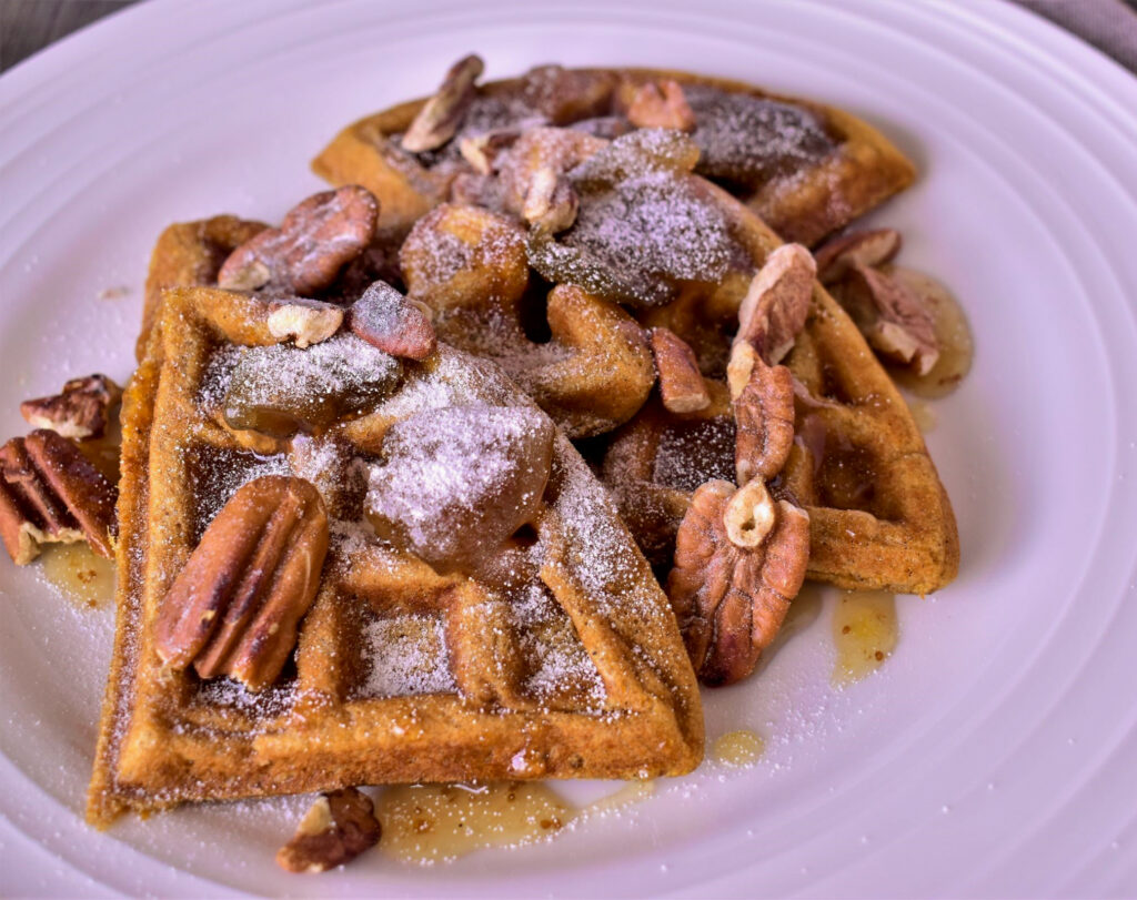 a close up of a plate of 3 sweet potato waffles with a buttery fig sauce on it