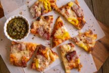 8 pieces of Tasso Flatbread Pizza scattered on parchment paper next to a container of Salsa verde