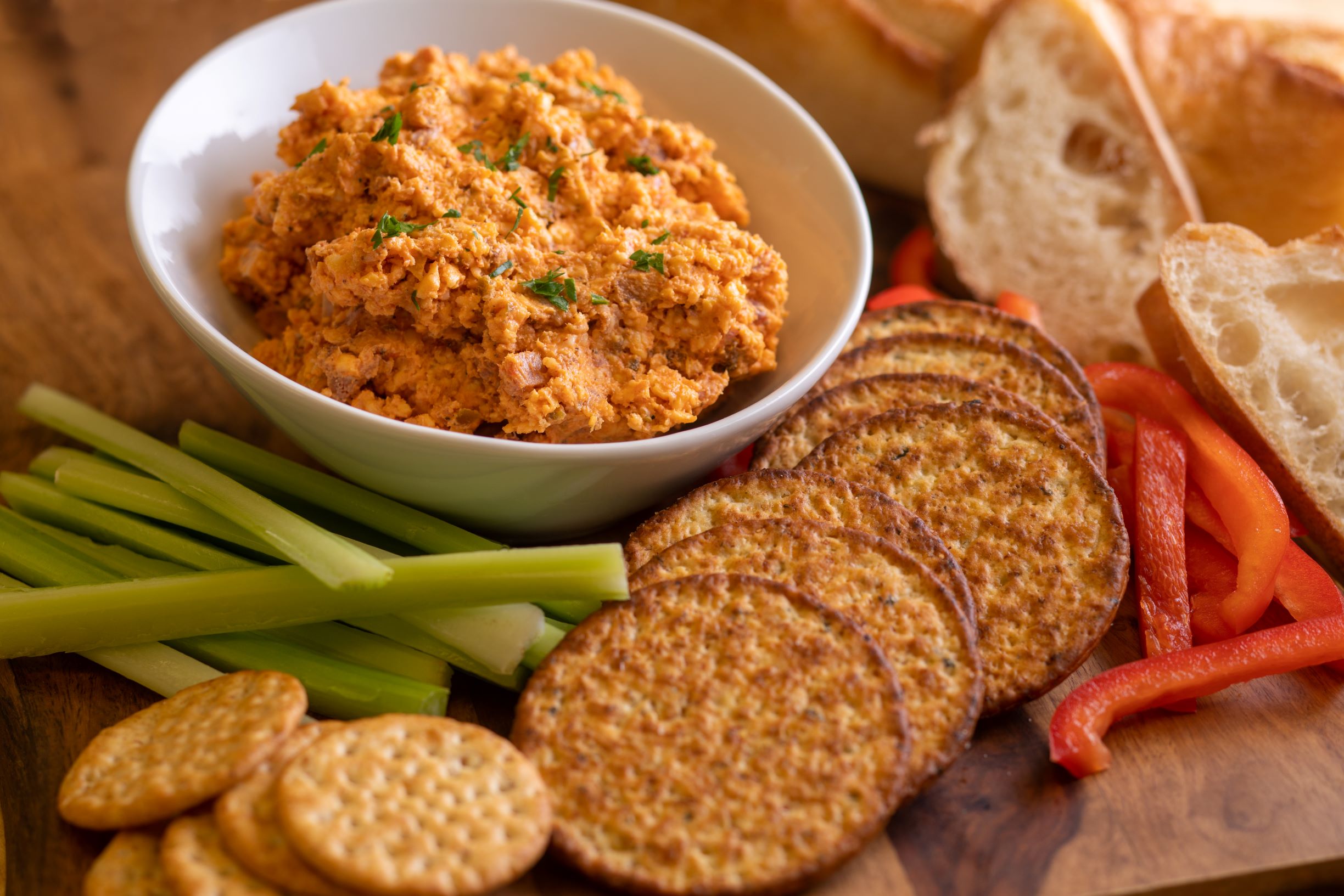 a bowl of tasso pimento cheese next to celery and carrot sticks, crackers and bread