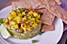 a plate with guacamole, shrimp and mango salsa stack with a lime slice and crackers