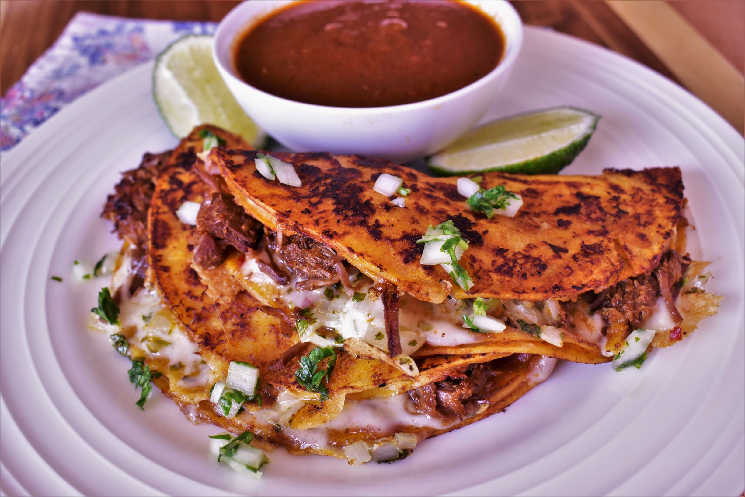 a plate of birria tacos and a dipping cup of salsa and 2 lime slices