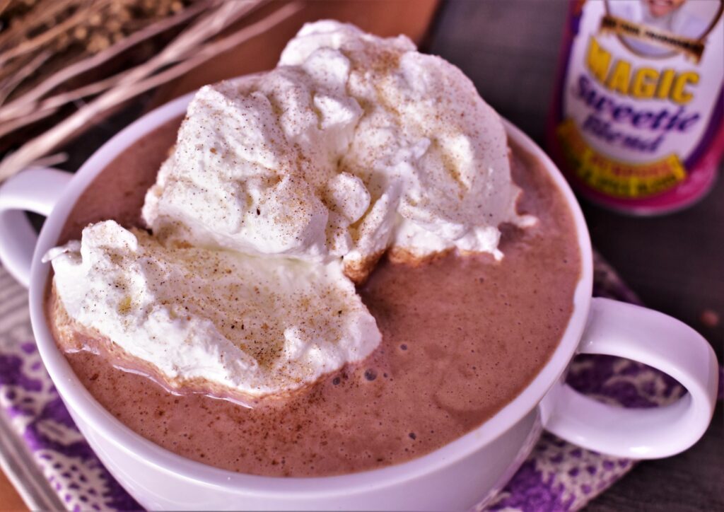 a cup of mexican hot chocolate topped with whipped creme and sweetie blend next to a container of magic swetie blend