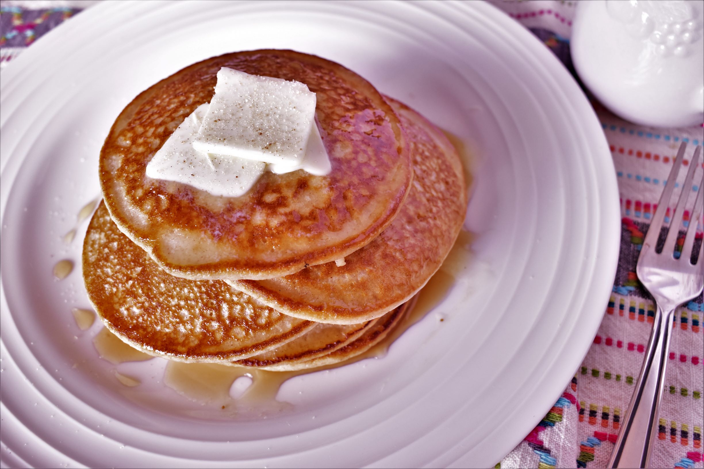 a plate of 5 oatmeal pancakes stacked on top of eachother with 2 squares of butter on top covered in syrup