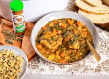 Turkey and fall vegetable stew in a bowl, with a bowl of wild rice, sliced rosemary bread, and a bottle of Chef Paul Prudhomme’s Poultry Magic.