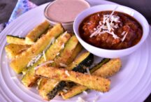 a plate of zucchini fries with a dipping cup full of dipping sauce and a small chilli