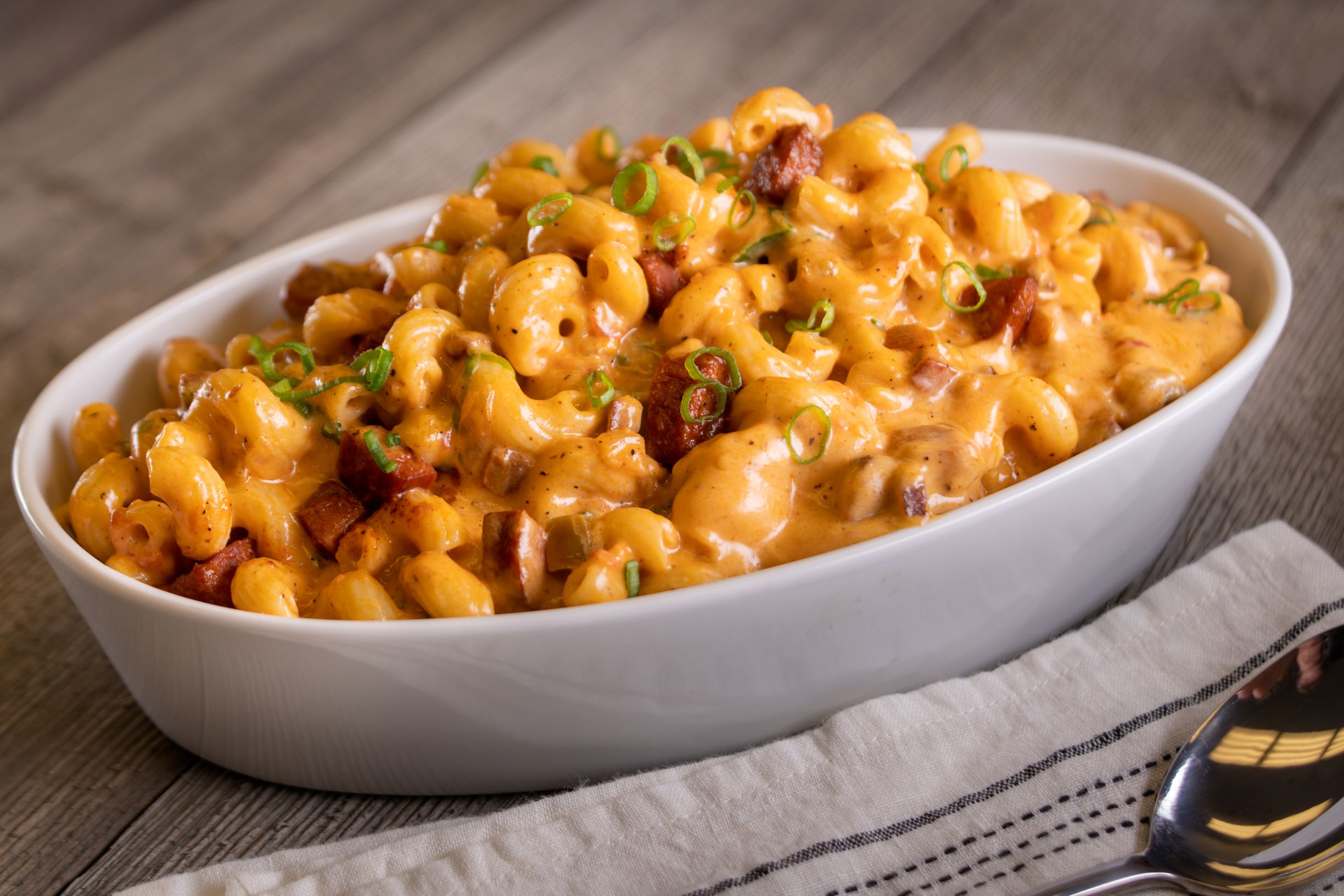 a serving bowl of cajun mac and cheese with a sausage and green onions