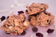 3 cranberry double chocolate chip cookies on a plate surrounded by chocolate chips and cranberries