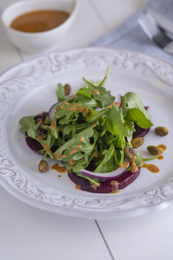 a plate of roasted beet and arugula salad next to a cup of salad dessing