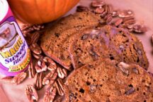 3 pieces of pumpkin pecan loaf with a caramel glaze next to a container of magic sweetie blend with pecans scattered all over the cut board