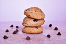 3 sweetie magic chocolate chip cookies stacked on top of eachother surrounded by sweetie magic and chocolate chips