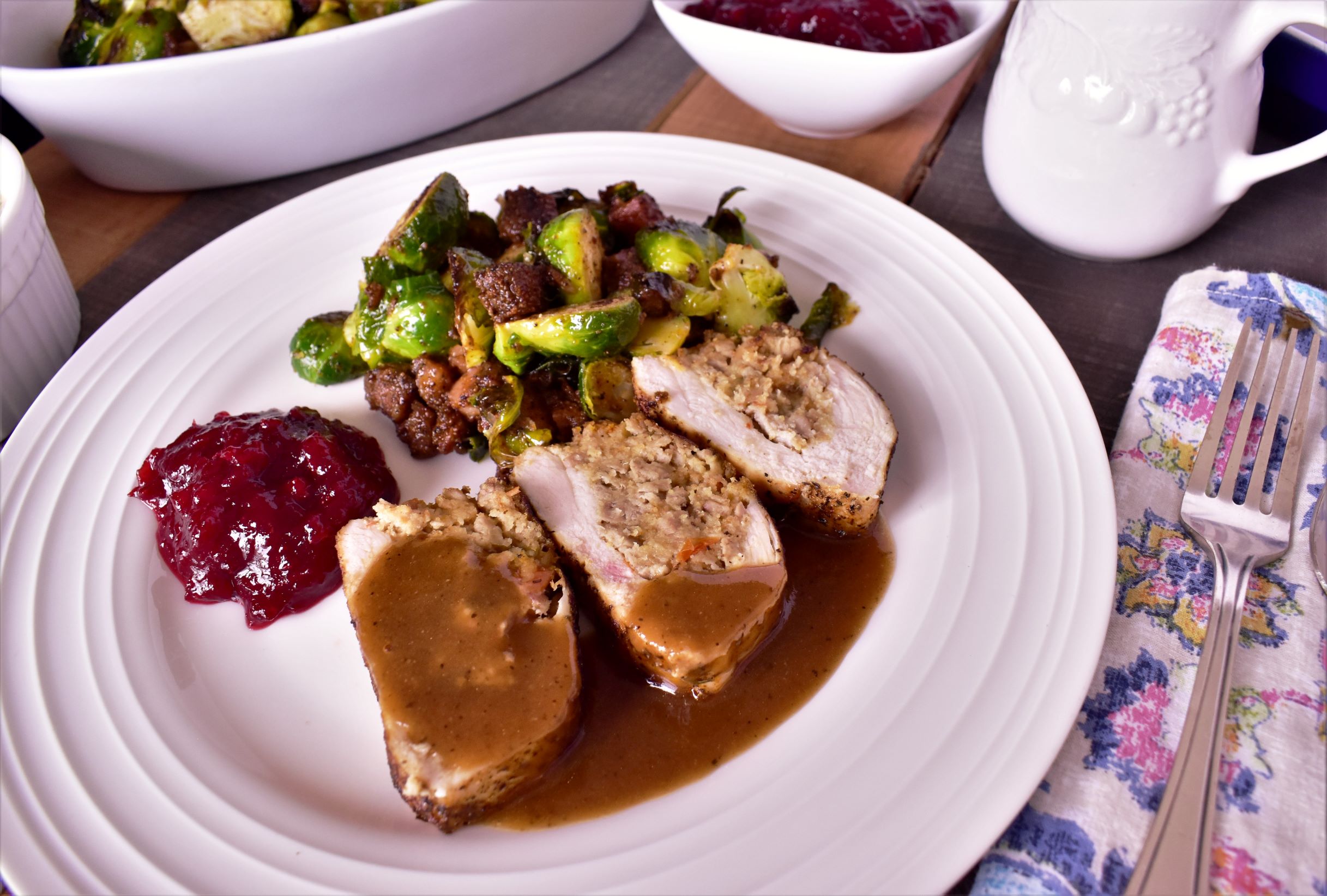 a plate of duck and cornbread stuffed chicken with turkey gravy, cranberry sauce and mixed veggies