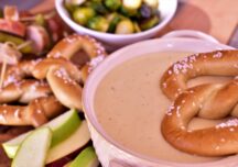 a bowl of beer cheese fondue next to twisted pretzles