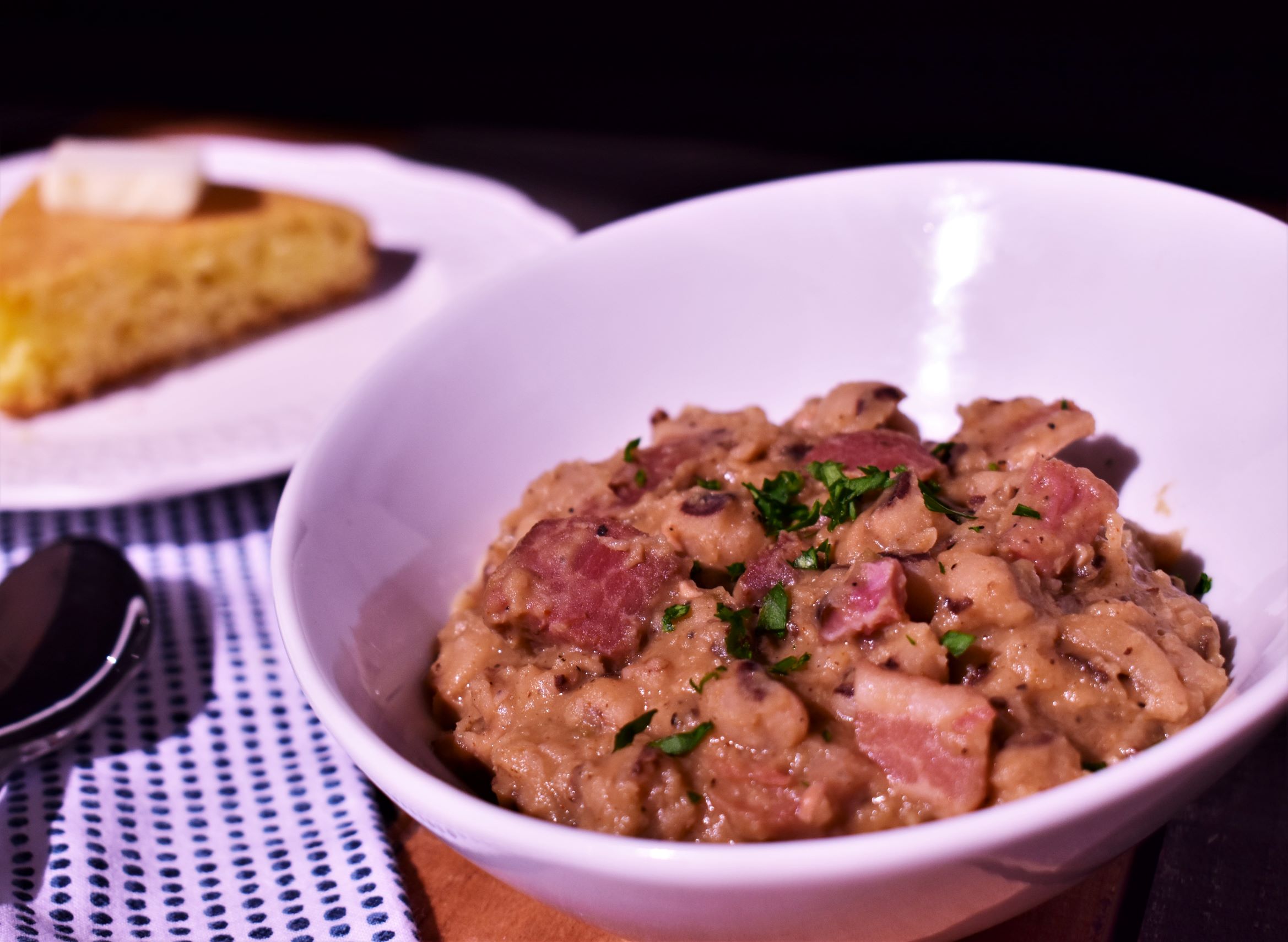 a bowl of black eyed peas with slab bacon and tasso next to a pice of corn bread edited version