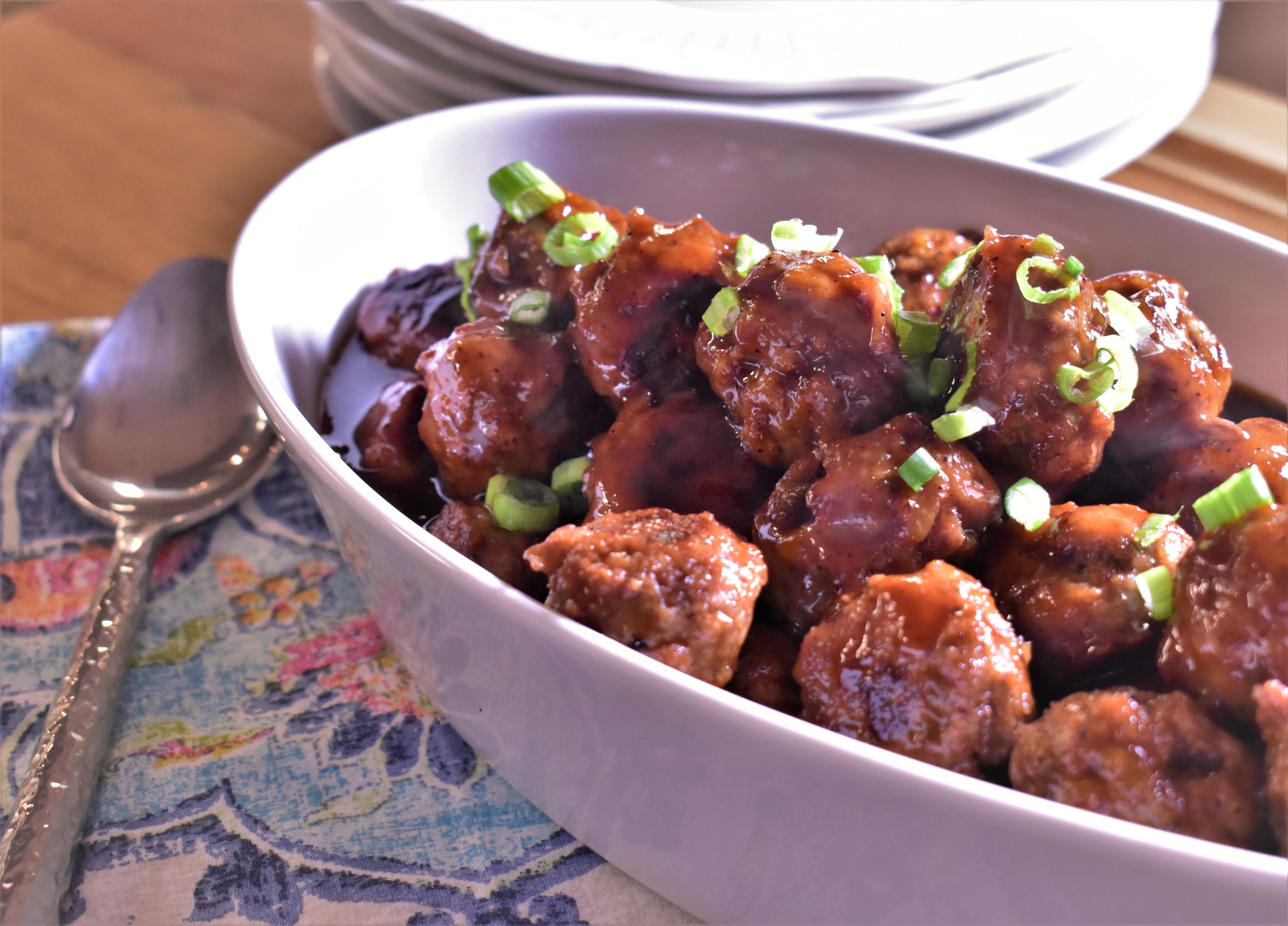 a bowl of sweet and tangy cocktail party meatballs with green onions on top