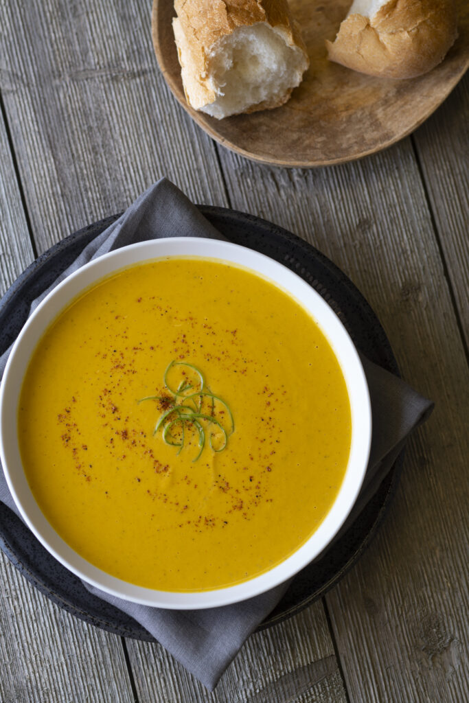 a bowl of curried sweet potato soup next to a plate of bread