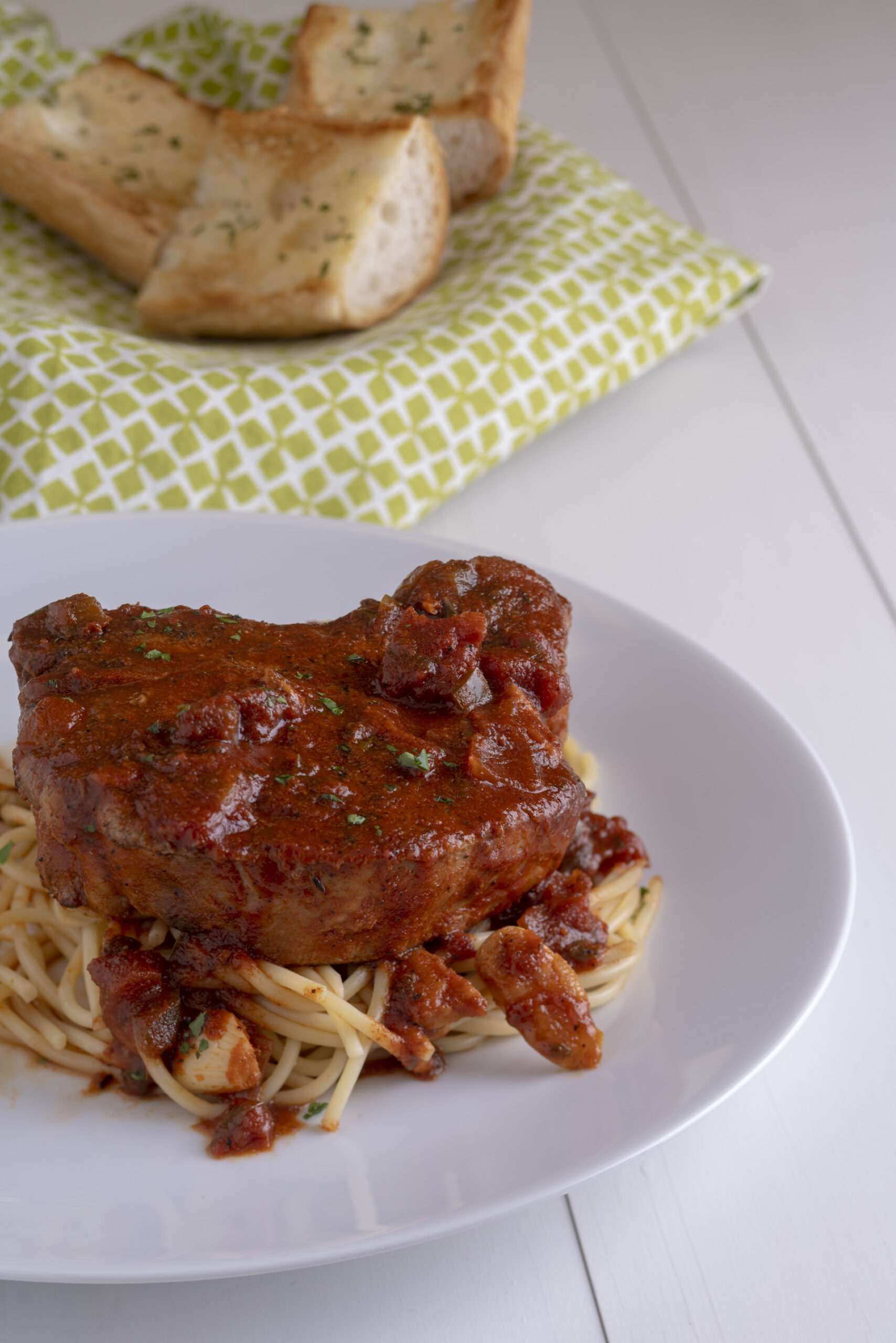 a plate of tomato braised pork chops with pasta and 3 pieces of garlic bread