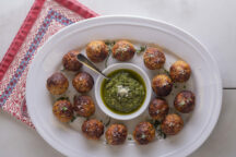 a serving tray full of chicken meatballs with a dipping cup full of pesto sauce