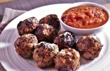 8 classic meatballs on a plate next to a dipping cup full of marinara sauce