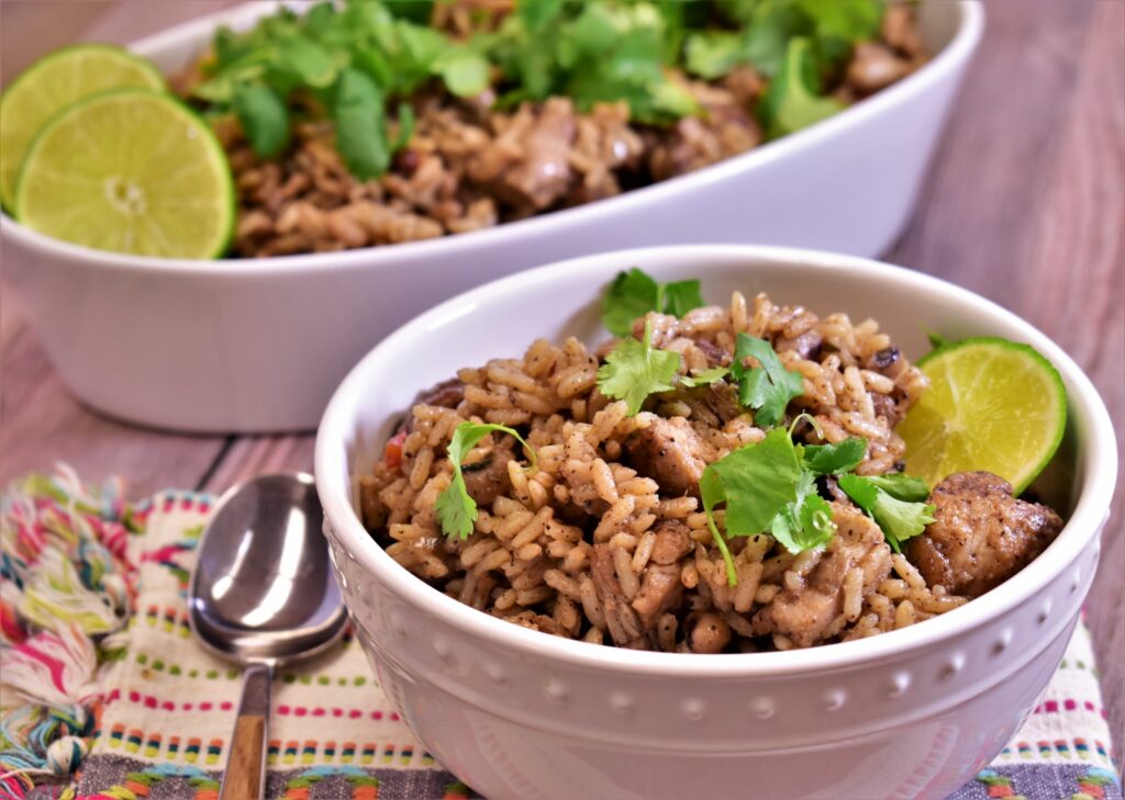 a bowl of jerk chicken, peas and rice with cilantro and lime slices