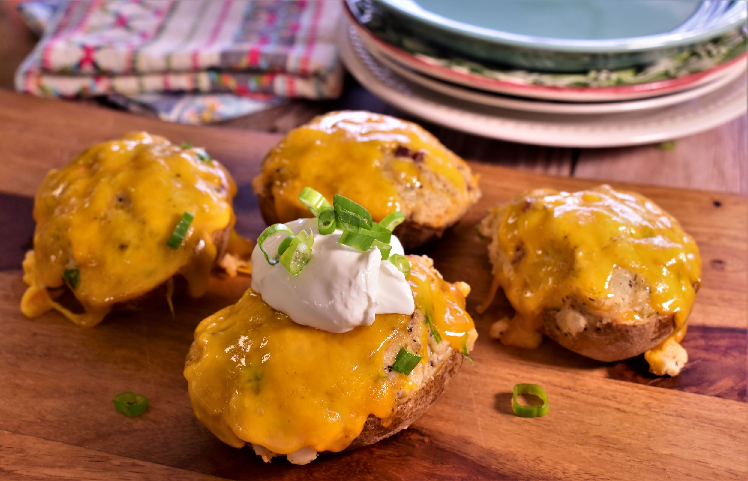 4 twice baked potatoes topped with cheese, a dallop of sour cream and green onions