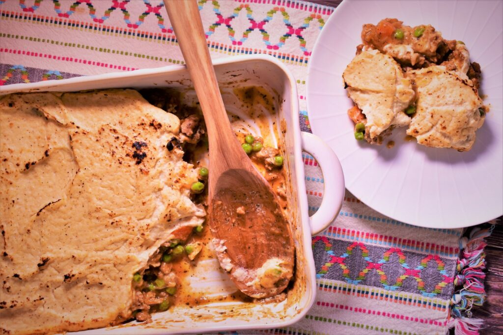 a piece of turkey cauliflower shepherds pie next to the half full container of shepherds pie