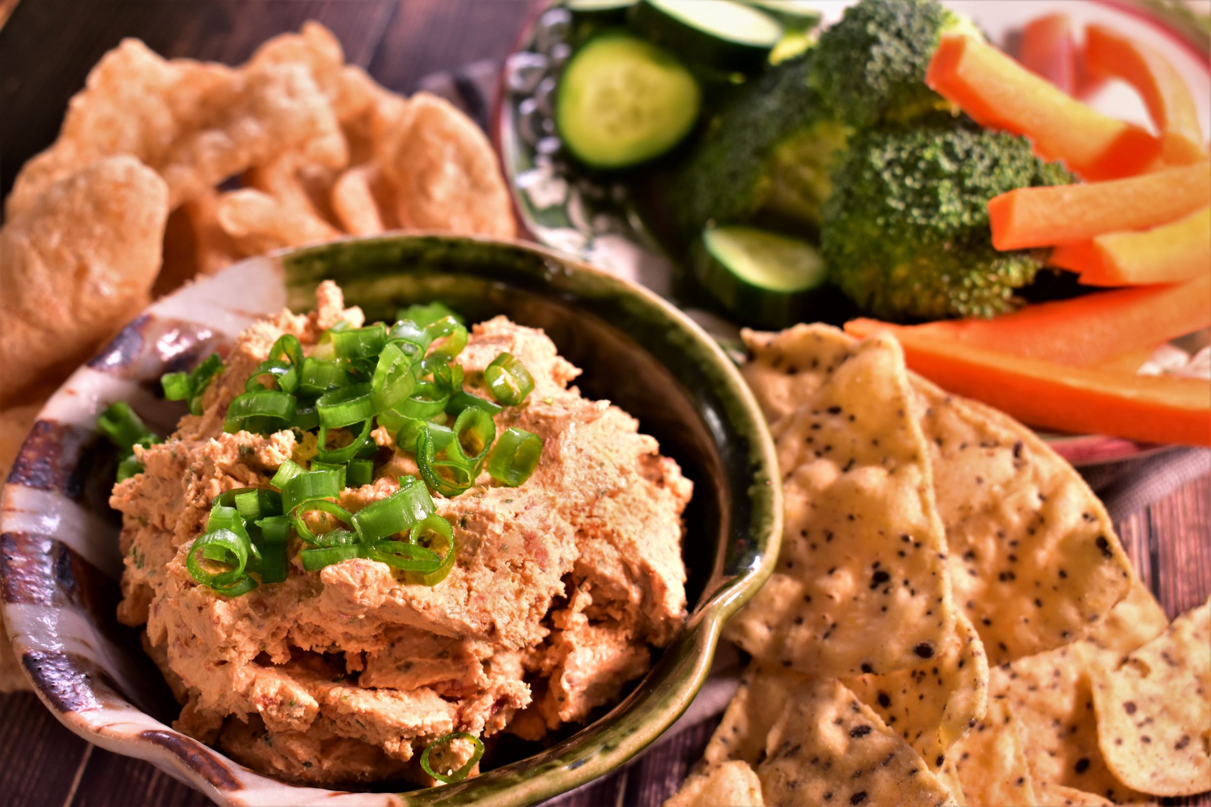 a close up of goat cheese dip topped with green oninions next to chips and various dipping vegetables