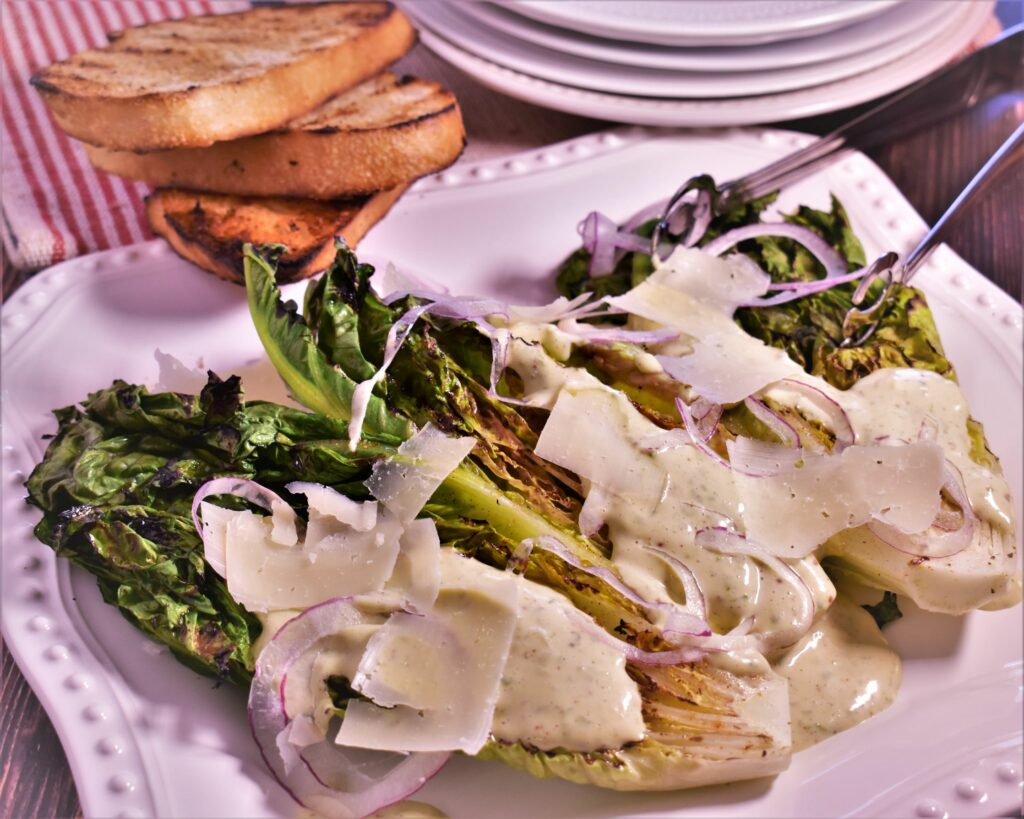 a plate of grilled romaine salad with 3 pieces of toasted bread on the side