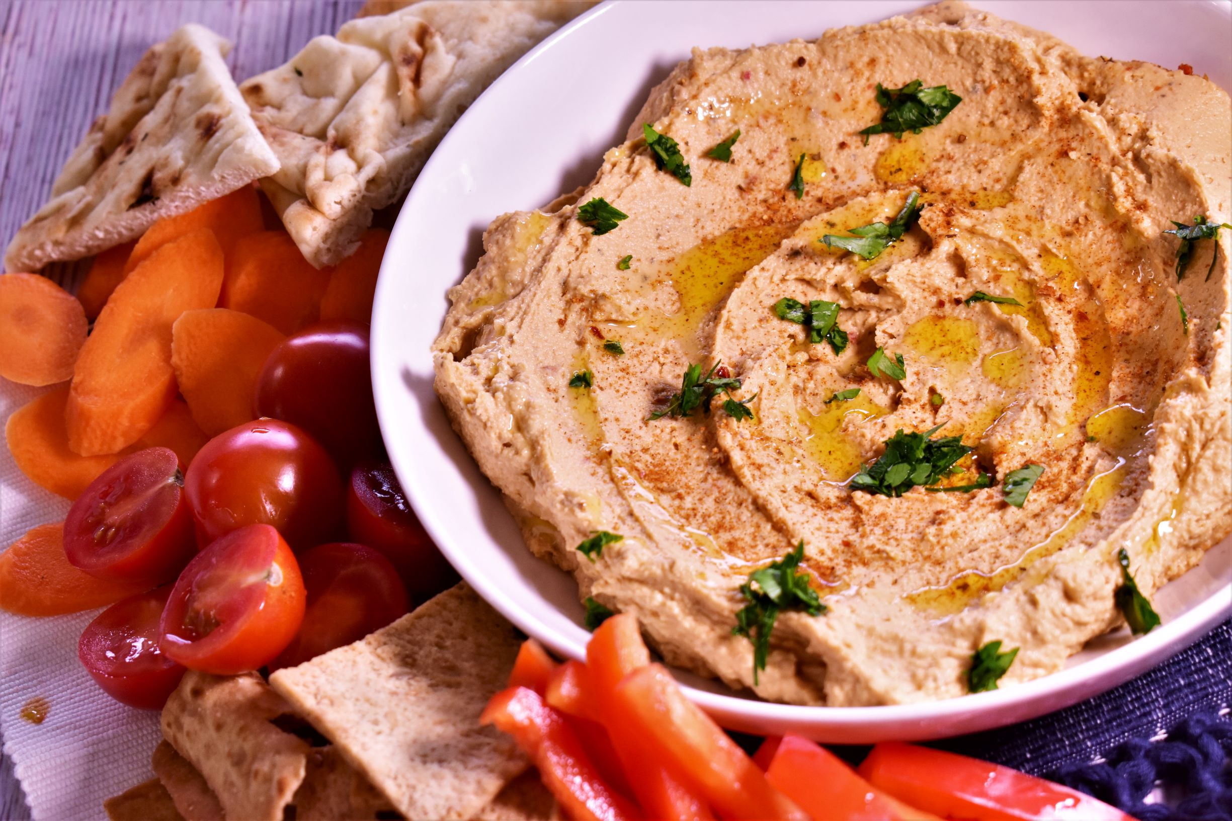 a bowl of hummas with drizzles of honey and basil next to pita bread, cherry tomatoes and other dipping veggies