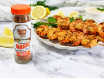 Shrimp Kabobs on a white plate next to a shaker of seafood magic seasoning and lemons
