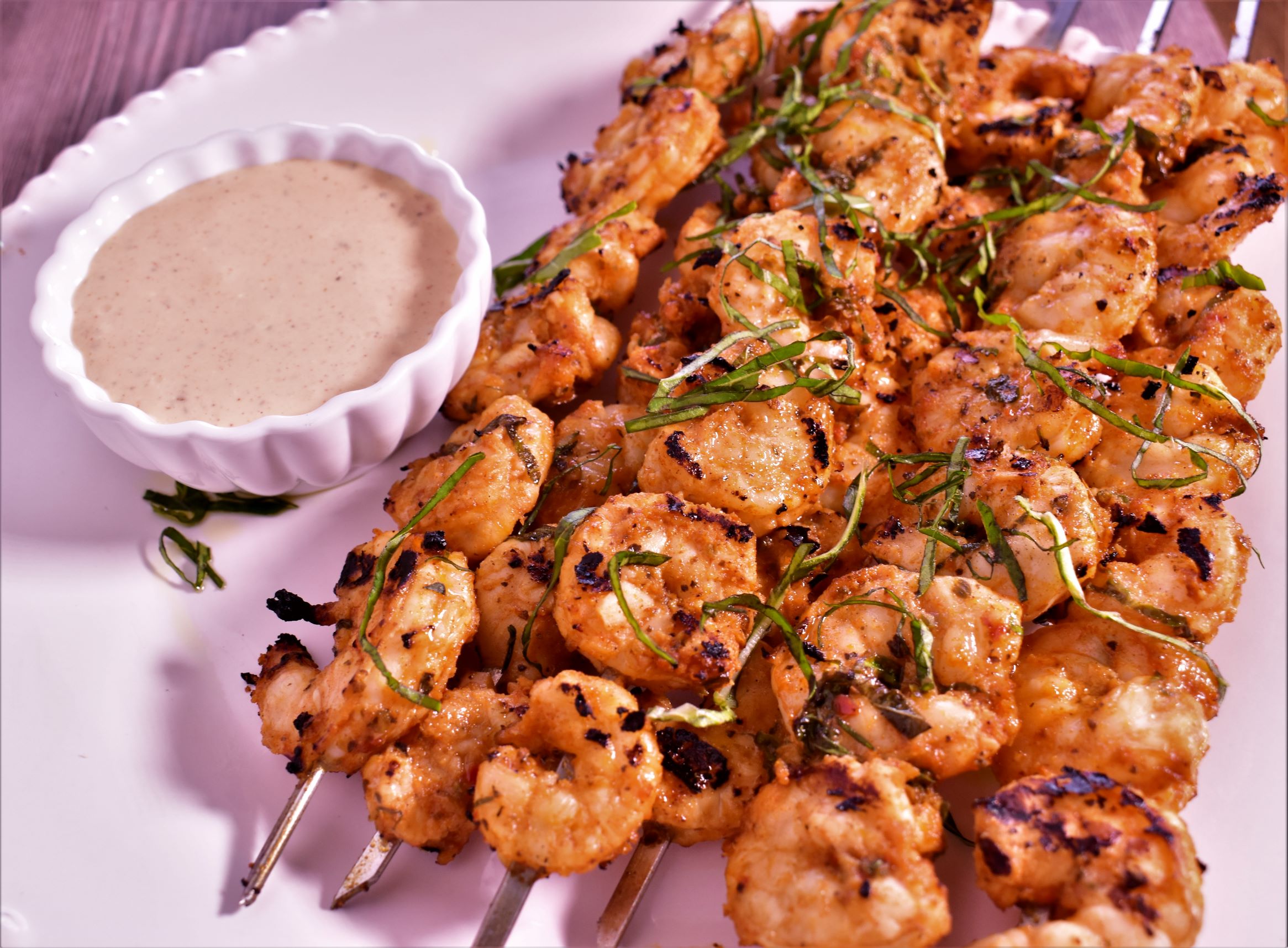 a plate full of 6 shrimp kabobs and a cup of dipping sauce