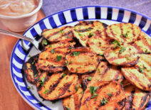A blue plate of grilled sweet potatoes next to a cup of dipping sauce