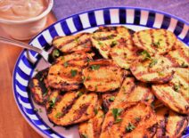 a plate of grilled sweet potatoes next to a cup of dipping sauce