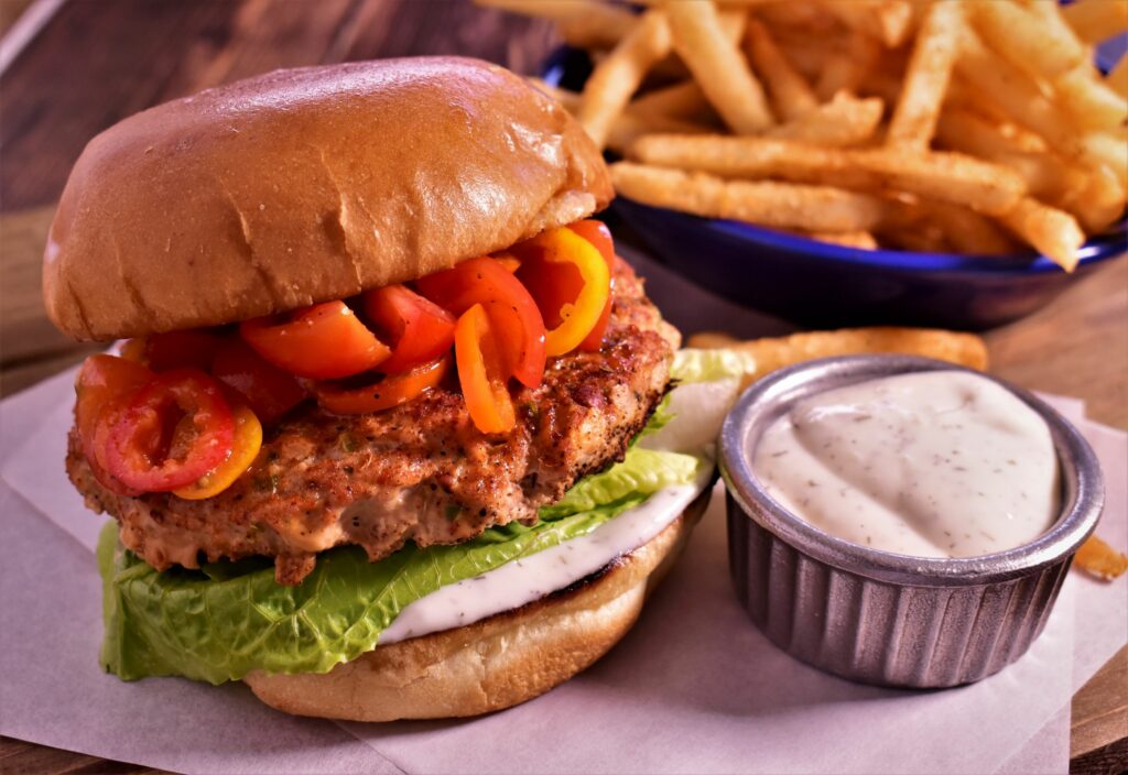 a new york styled turkey burger dressed with red and orange bell pepeprs, lettuce and mayo with a side of fries and a dipping cup of sauce