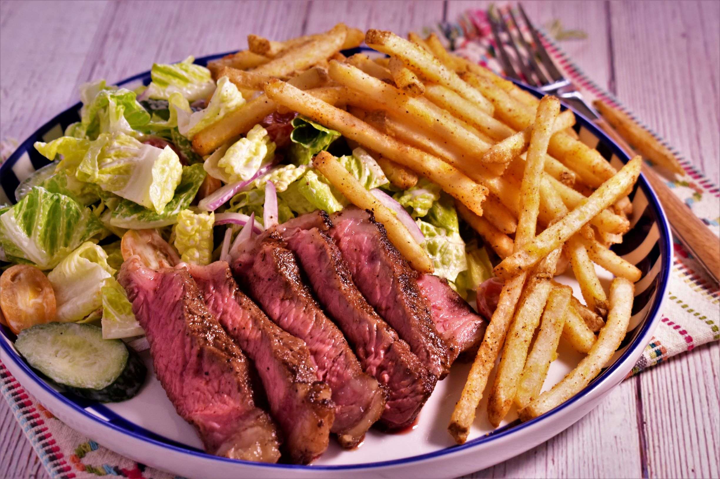 a pittsburgh steak salad with 6 pieces of steak cooked medium well and a side of seasoned fries
