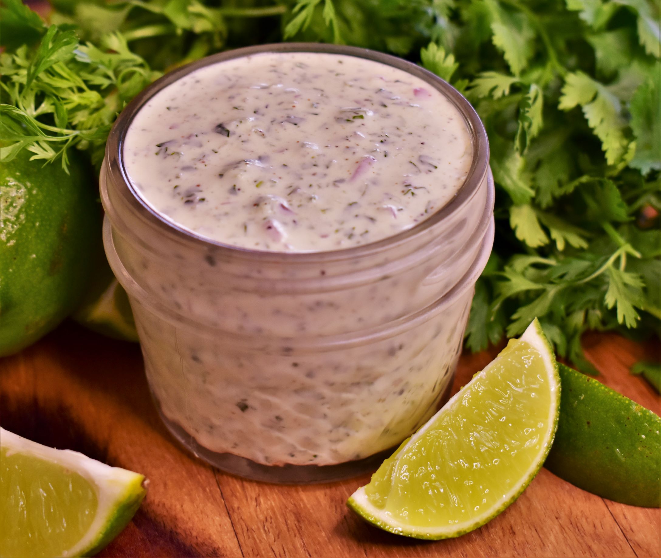 a cup of cilantro lime tartar sauce next to a bunch of cilantro and a few lime slices