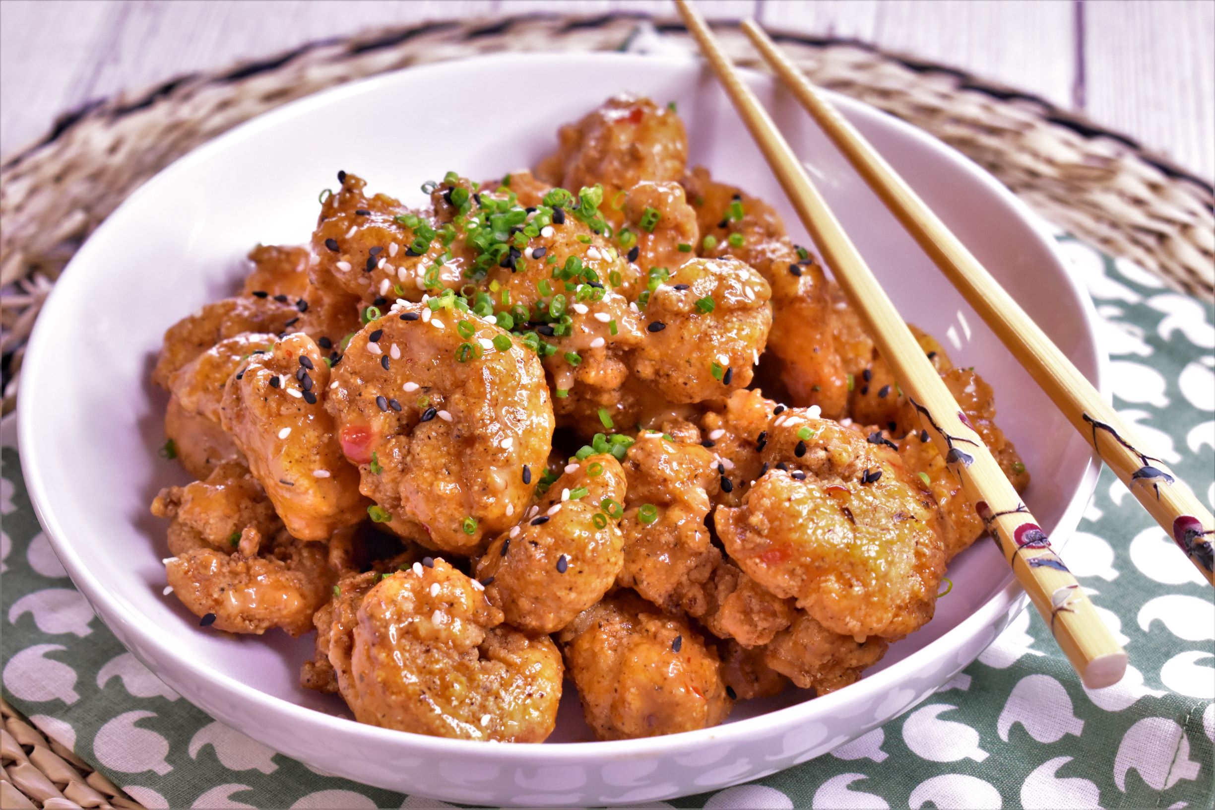 a bowl of dynamite shrimp bang bang topped with green onions with a nice pair of chopsticks on top the bowl